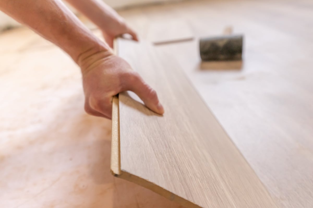 Worker installing laminate flooring planks over underlayment