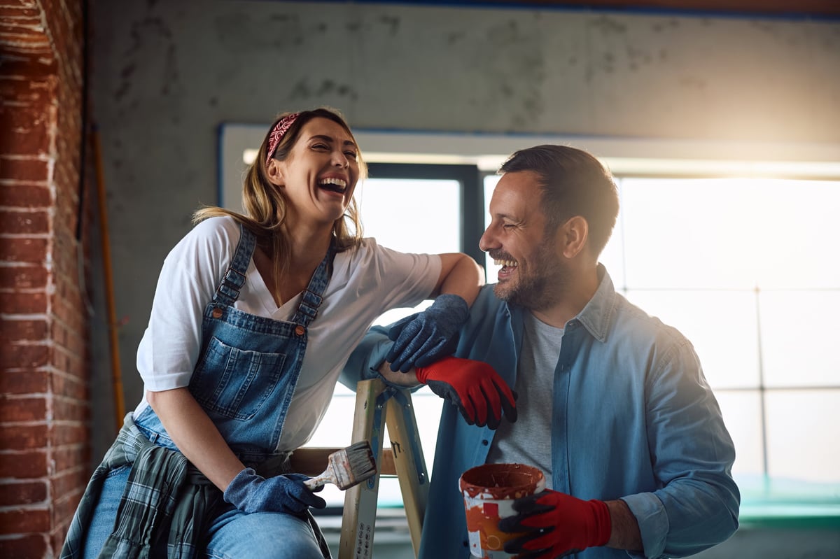 Happy couple laughing while painting walls during a home remodel